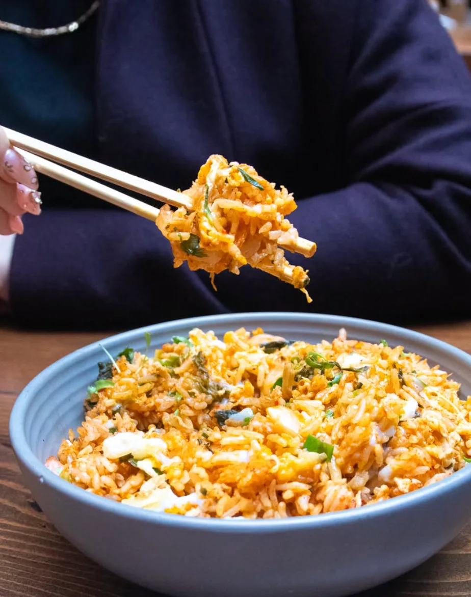 Bowl of vibrant orange fried rice with a hand lifting a chopstickful above the dish.